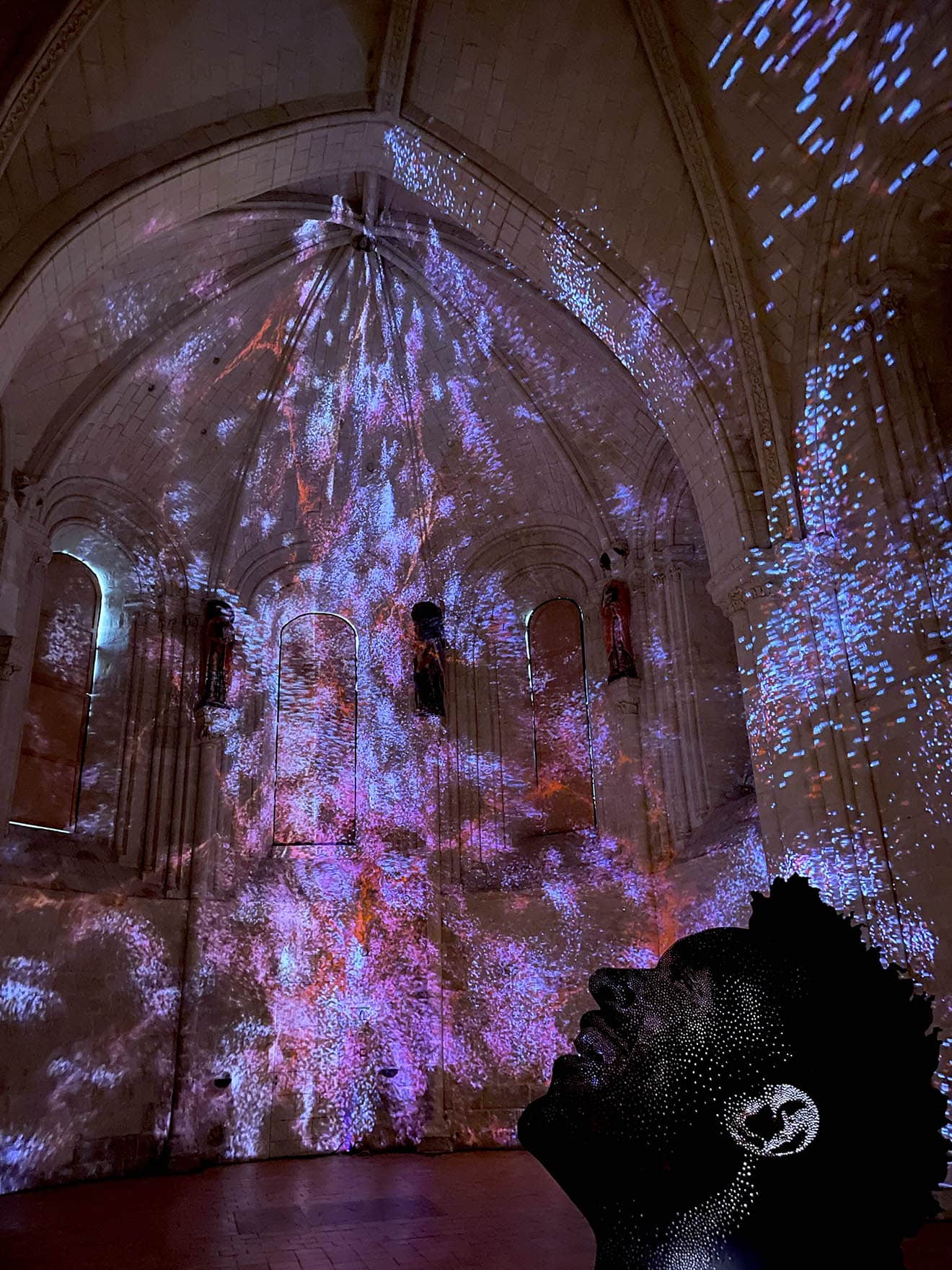 Dark cathedral with small purple, red and blue lights shining on the walls and ceiling, outline of a person looking up and smiling.